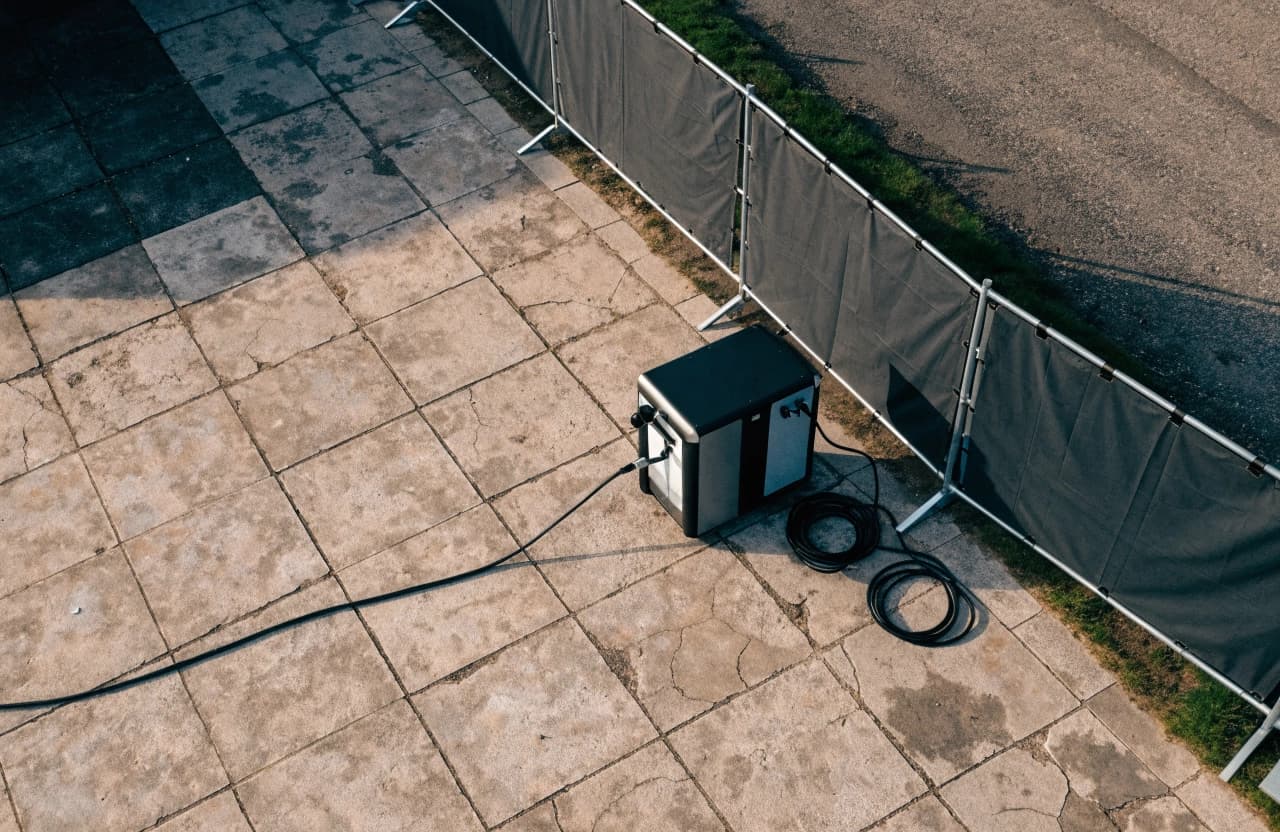 Eine kompakte mobile Ladestation auf einem Platz nahe eines temporären Bauzauns.